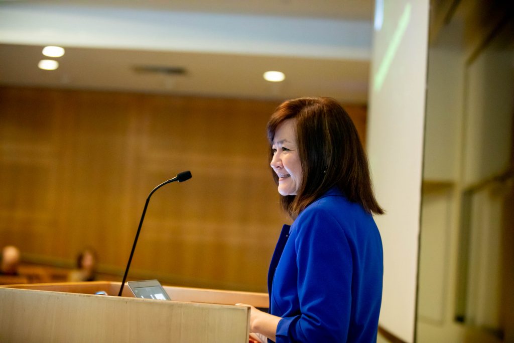 Li-Huei Tsai is shown in profile as she stands smiling at a podium